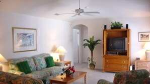 A living room with a sofa, armchairs, a coffee table, a television on a wooden cabinet, a ceiling fan, and a potted plant. - Ahr137 - Tuscan Hills - 4 Bed 3 Baths Villa (Davenport)