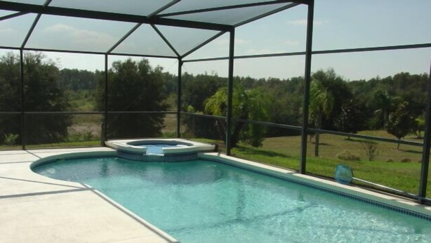 A swimming pool with a hot tub, surrounded by a glass enclosure, and a view of a green landscape. - Ahr137 - Tuscan Hills - 4 Bed 3 Baths Villa (Davenport)