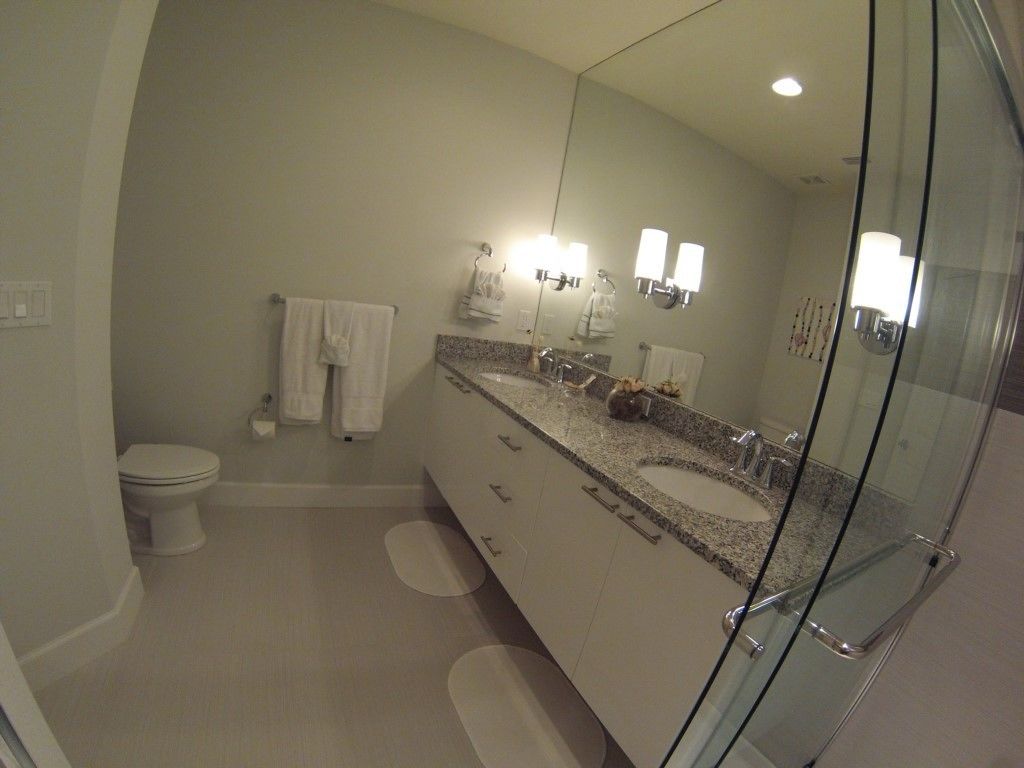 Une salle de bain moderne avec une douche à l’italienne en verre, un grand meuble-lavabo avec un plan de travail en granit et des toilettes blanches.