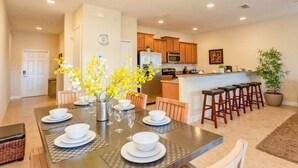 A modern kitchen with wooden cabinets, a central island, and a dining area with a table set for four. - Fv46473 - Paradise Palms - 4 Bed 3 Baths Townhome (Kissimmee)