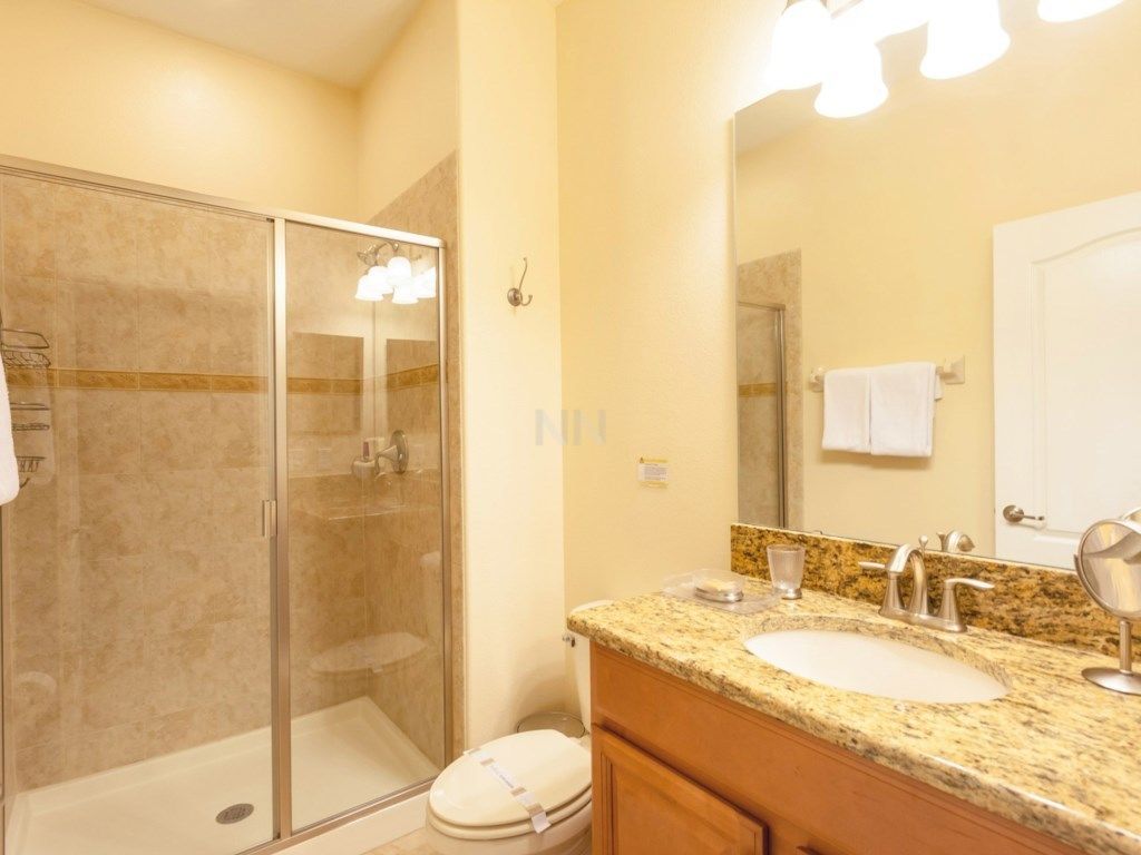 A bathroom with a glass shower enclosure, a sink with a granite countertop, and a mirror above the sink.