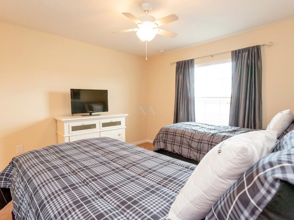 A bedroom with two beds, a TV on a dresser, and a ceiling fan.