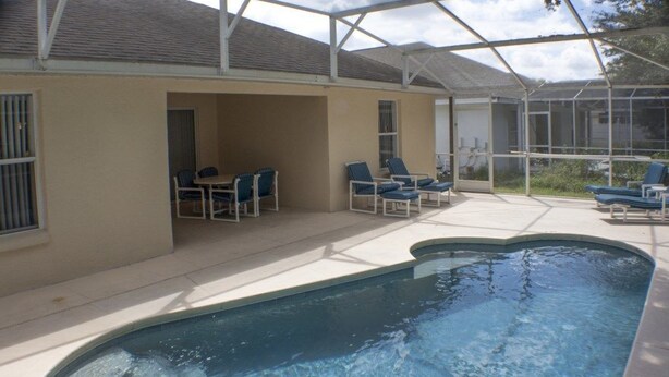 A covered outdoor swimming pool area with lounge chairs and a table. - Ip60179 - Silver Creek - 4 Bed 3 Baths Villa (Clermont)