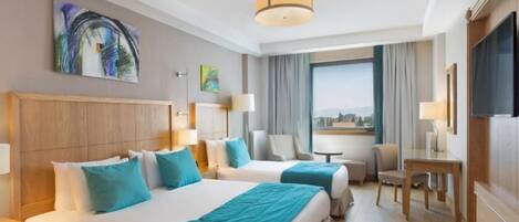 Habitación de hotel con dos camas, un escritorio, una silla, un televisor y una ventana con vistas a la ciudad.