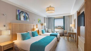 A hotel room with two beds, a desk, a chair, a TV, and a window with a city view. - Plus Hotel Setif (Setif)
