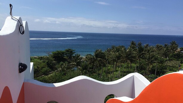 A coastal view with a white and orange building, palm trees, and the ocean. - Fuyue sea View (Taitung)