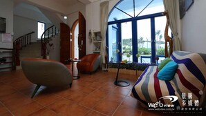 A spacious living room with a large window, a staircase, and a sofa with striped cushions. - Fuyue sea View (Taitung)