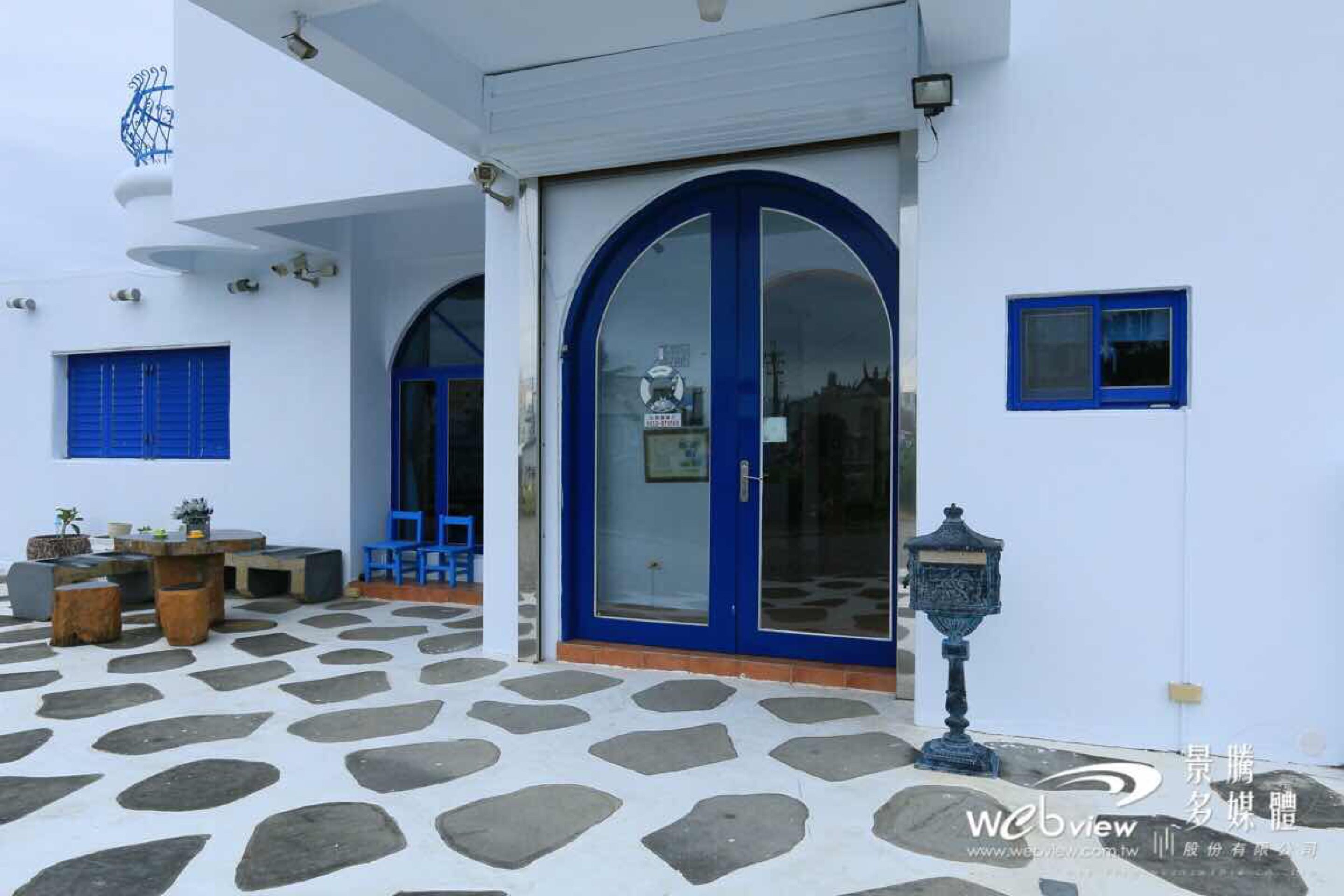 A building with a white exterior, a blue door, and a stone-patterned patio.