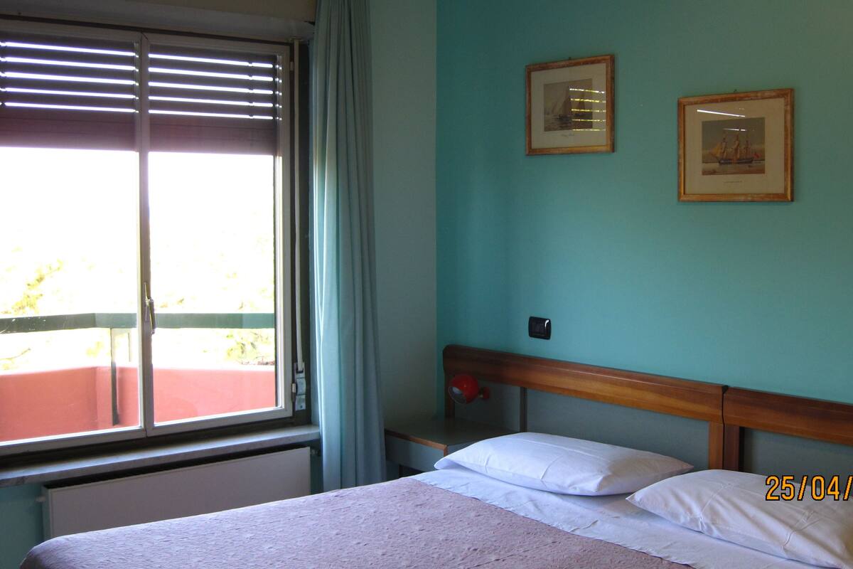 Un dormitorio con una cama, una ventana con persianas y dos cuadros en la pared.