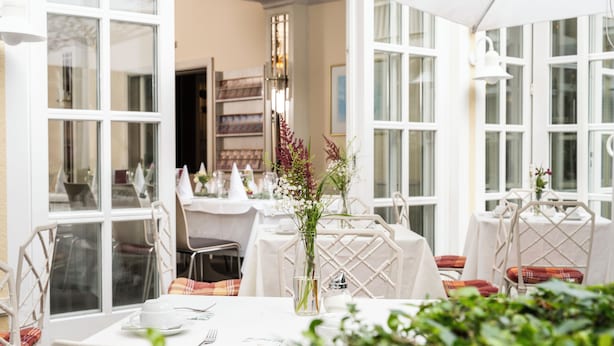 A dining area with tables set for two, white tablecloths, and chairs with plaid cushions.