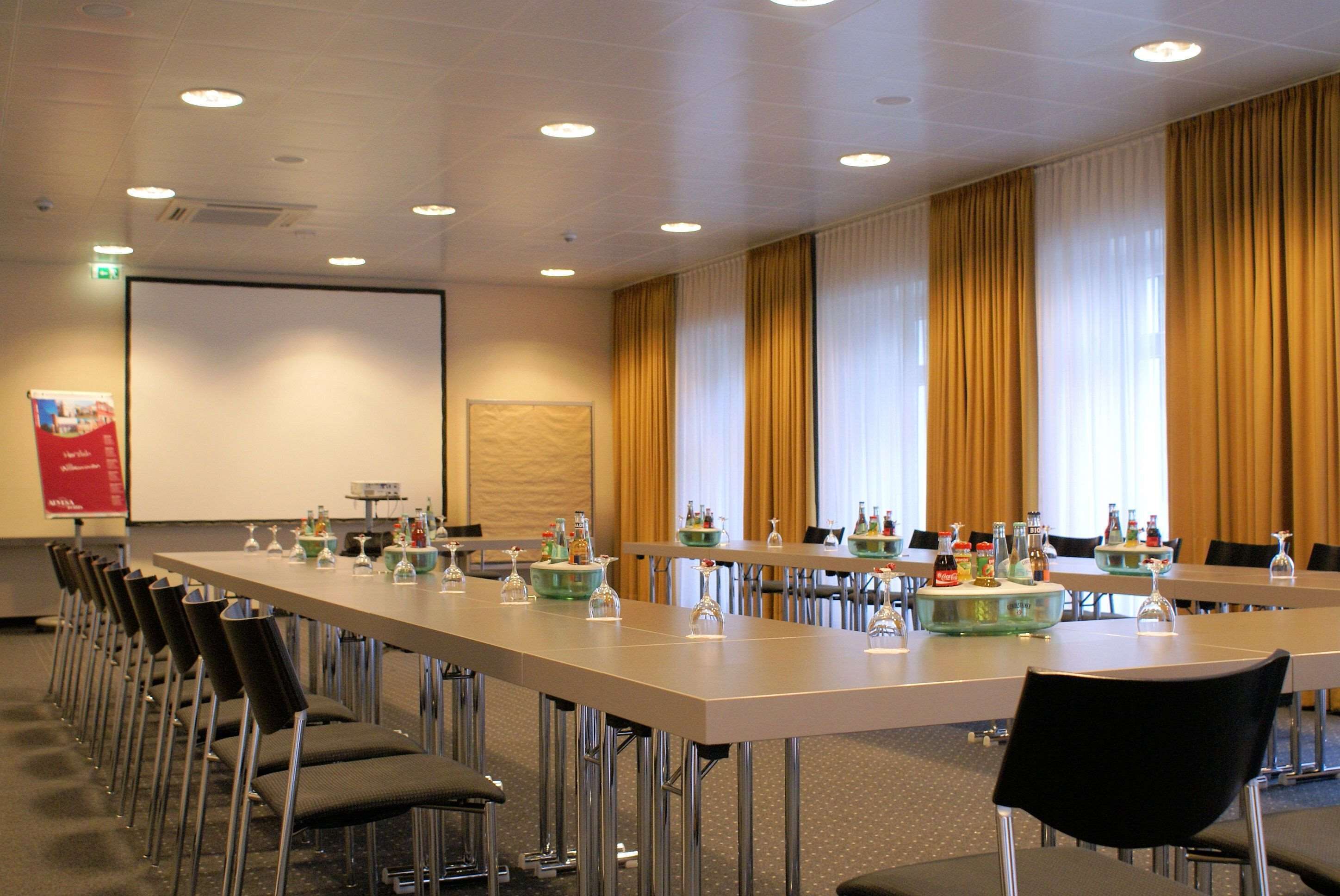 Une salle de conférence équipée de longues tables, de chaises et d’un écran de projection.