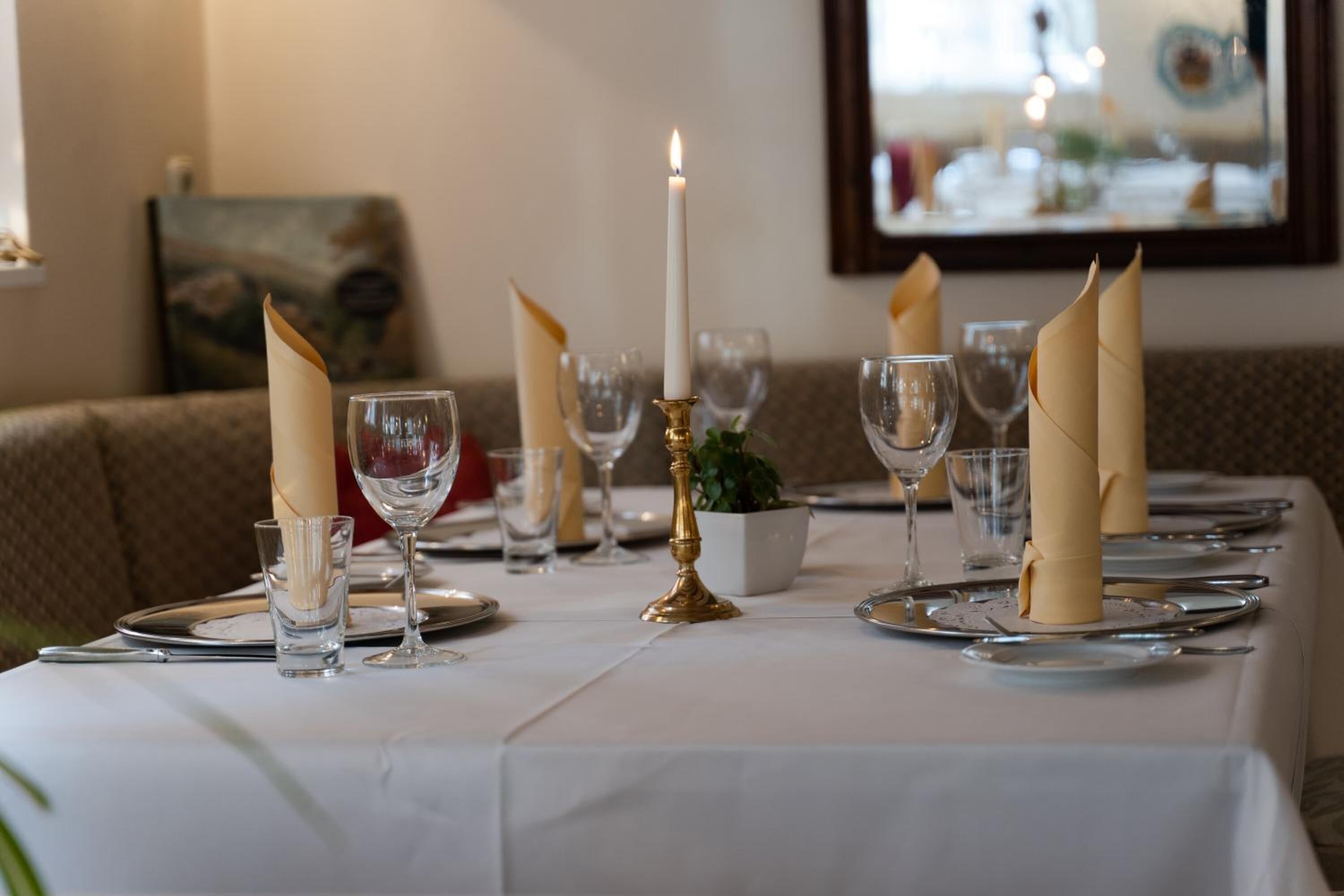 A dining table set with white tablecloth, candles, and folded napkins.