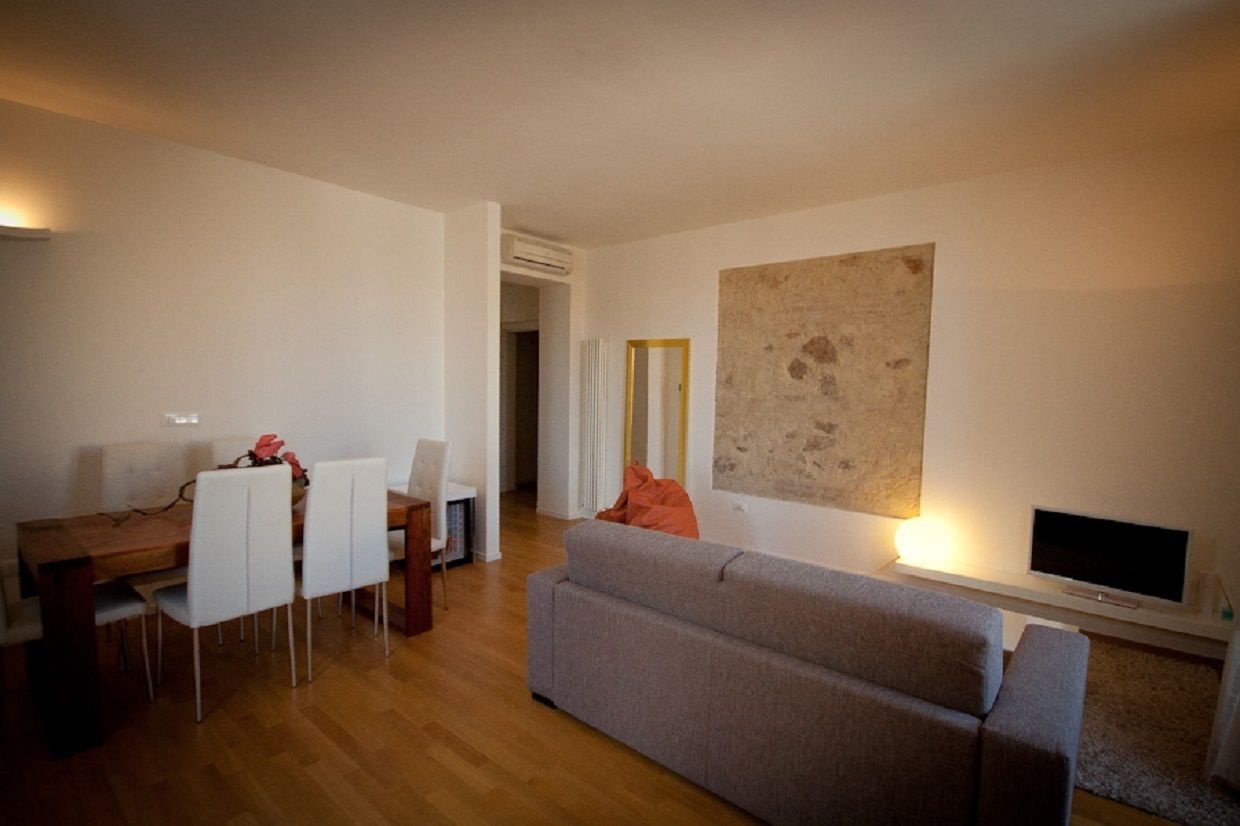 A modern living room with a grey sofa, a dining table with chairs, a TV, and a large abstract painting on the wall.