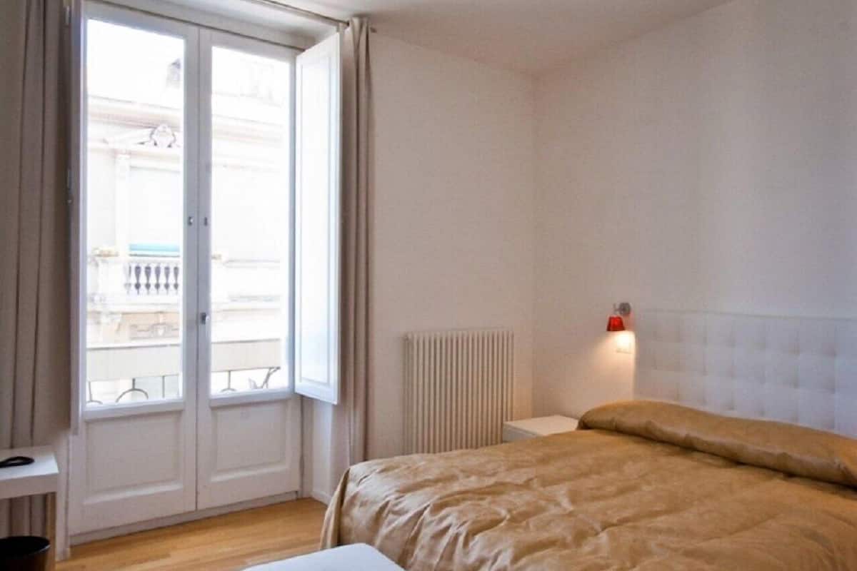 Ein Schlafzimmer mit einem Bett, einem Heizkörper, einem Fenster mit Vorhängen und einem weißen Nachttisch.