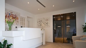 A modern reception area with a white reception desk, abstract art on the walls, and a glass door leading to another room. - Hotel Muraglie (Vibo Valentia)