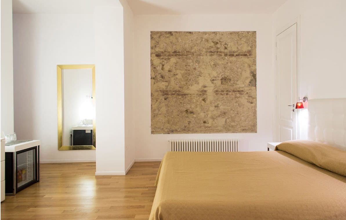 A bedroom with a bed, a mirror, and a large textured artwork on the wall.