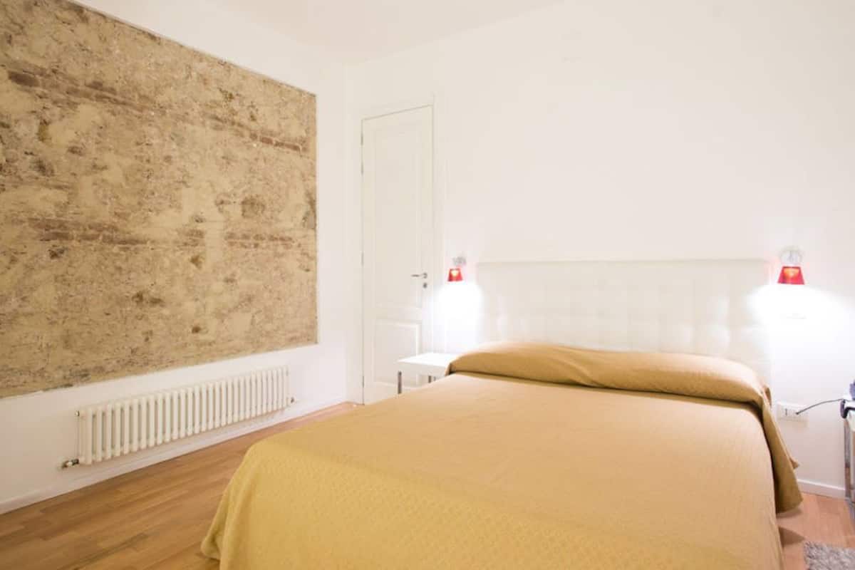 Ein Schlafzimmer mit einem großen, abstrakten Gemälde, einem Bett mit beiger Bettdecke, einem weißen Heizkörper und zwei Nachttischlampen.
