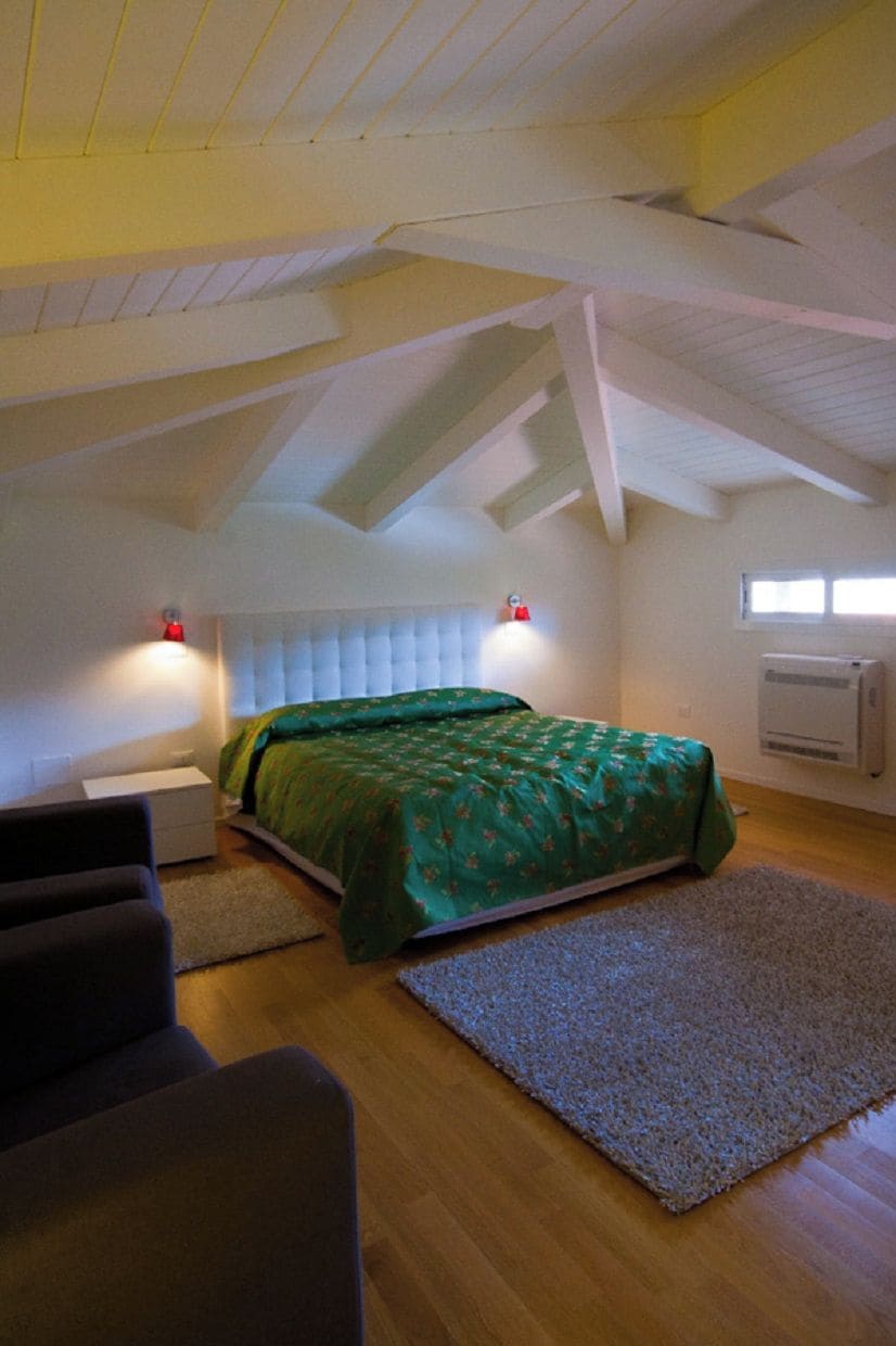 A bedroom with a bed, a nightstand, a chair, a rug, and a window with an air conditioner.