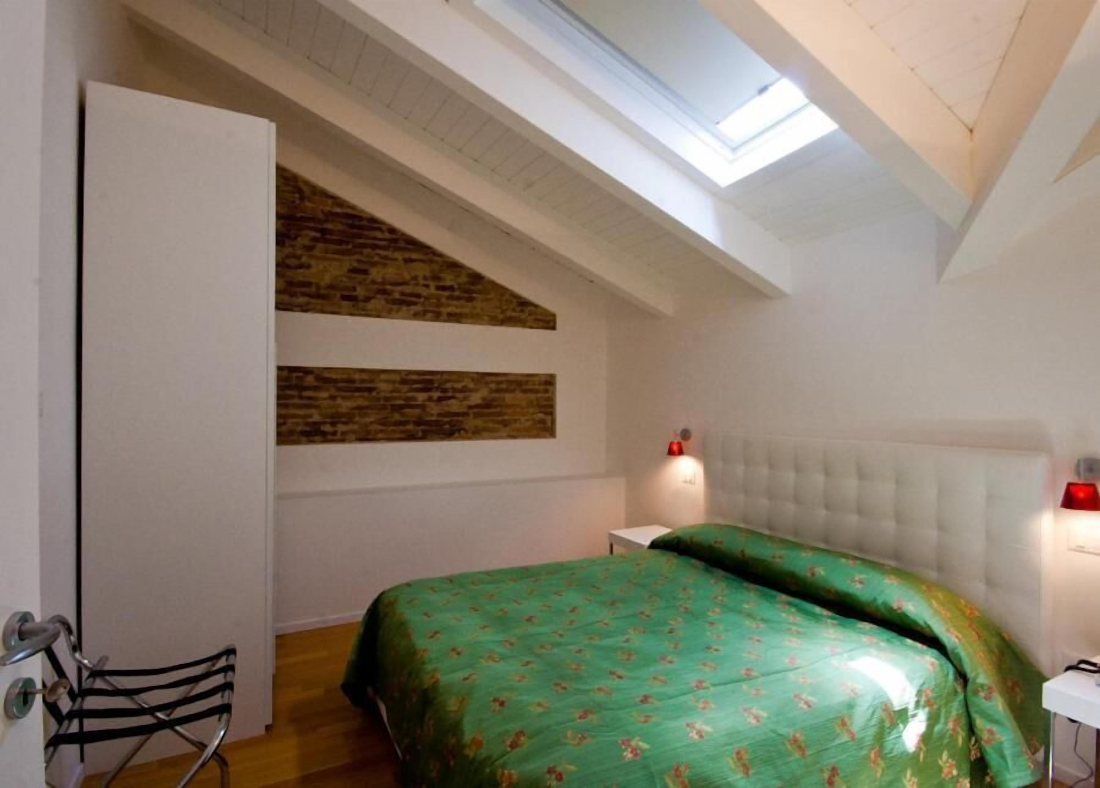 A bedroom with a sloped ceiling, a bed with green floral bedding, a white headboard, and a wall-mounted light fixture.
