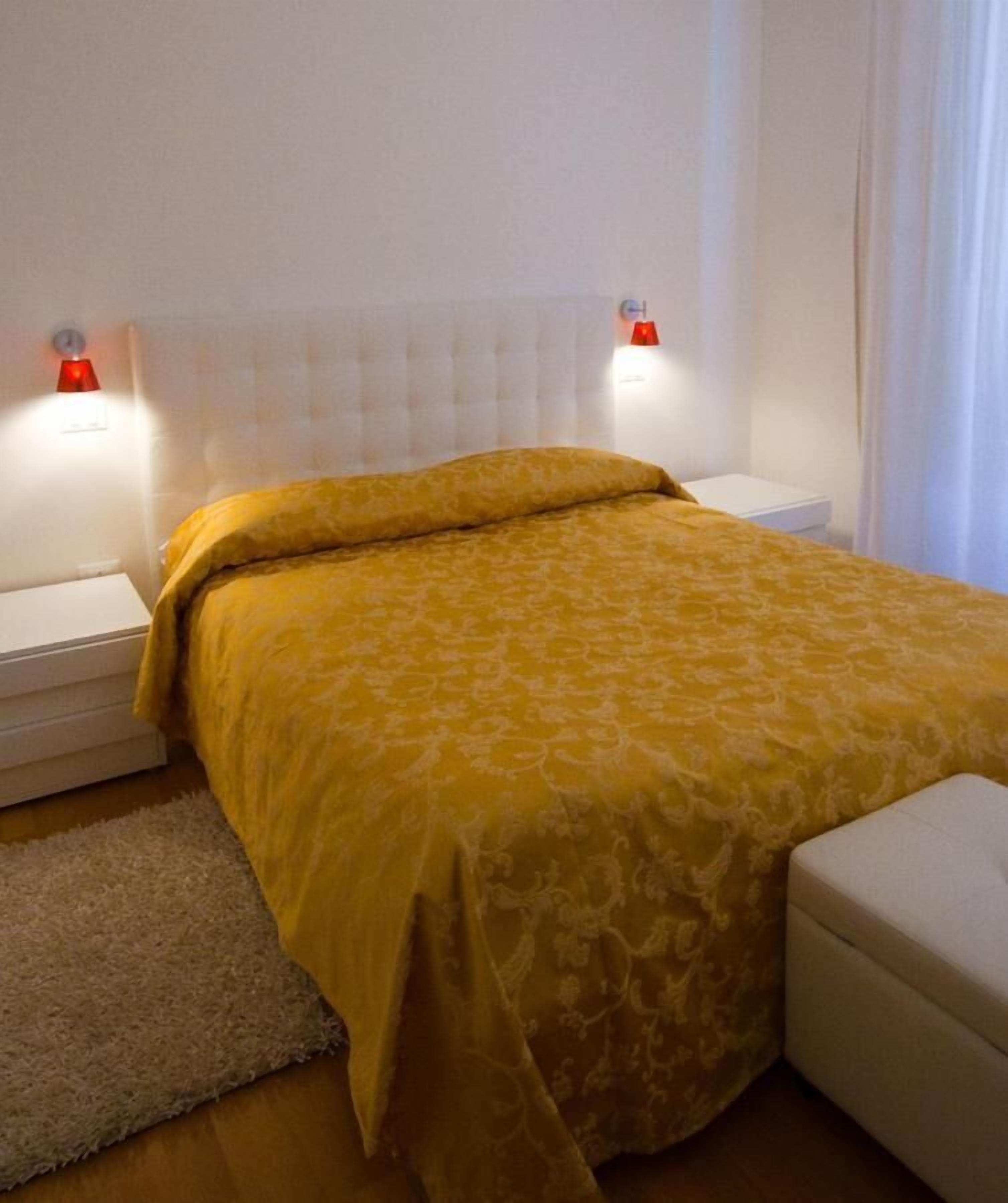 A bedroom with a large bed, two bedside tables, a white headboard, and a white nightstand.