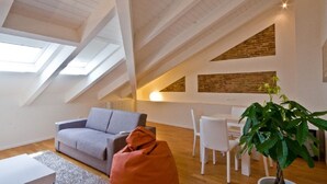 A modern loft with a sloped ceiling, skylights, a gray sofa, white dining chairs, and a potted plant. - Hotel Muraglie (Vibo Valentia)