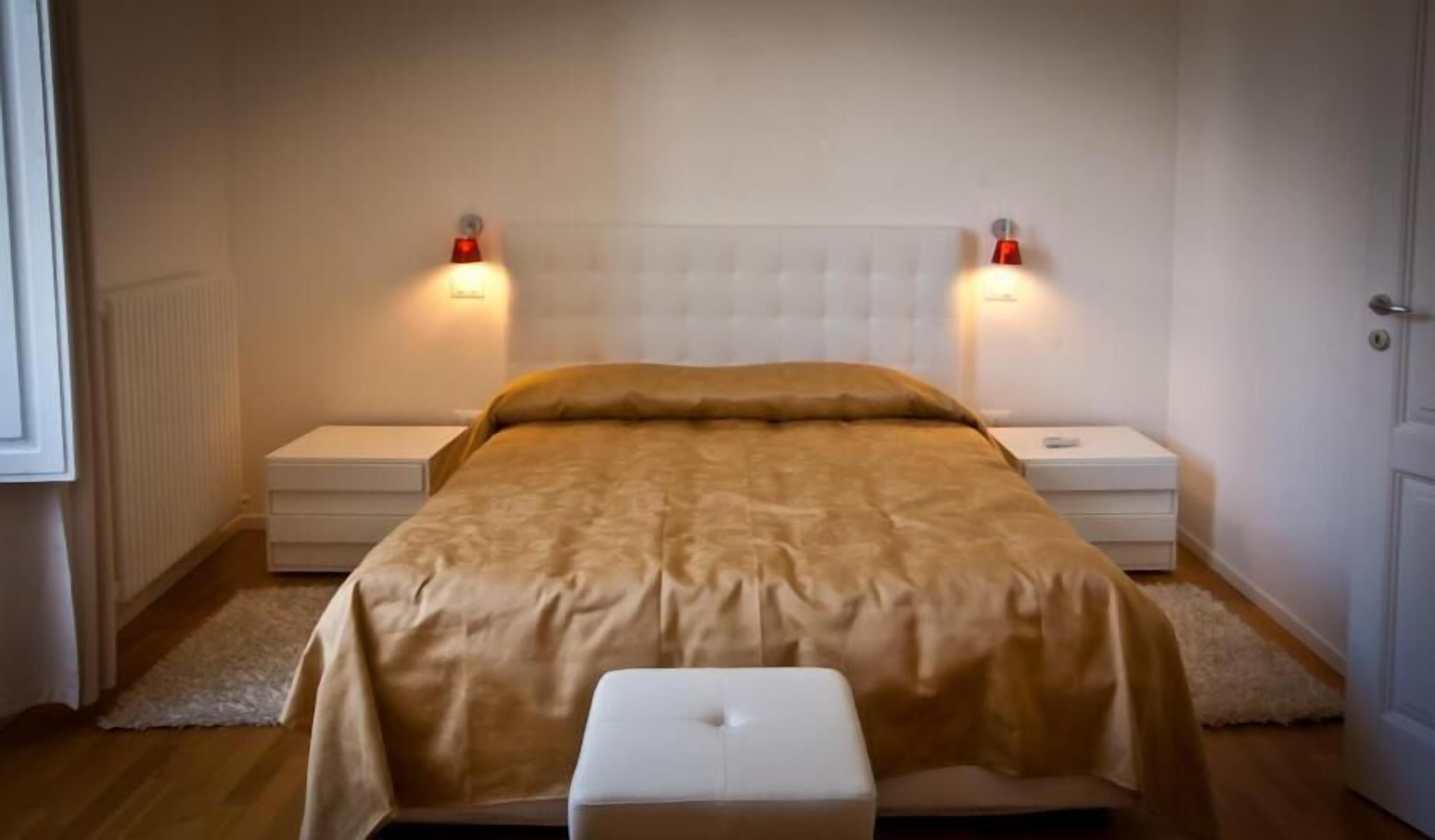 Ein Schlafzimmer mit einem Bett, zwei Nachttischen, einer Bank und zwei Wandlampen.