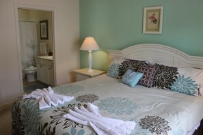 Cama bem arrumada com roupa de cama florida, abajur e quadro na parede.