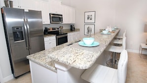 A modern kitchen with white cabinets, stainless steel appliances, a granite countertop, and bar stools.