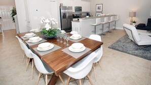 A modern kitchen with white cabinetry, stainless steel appliances, and a bar area with white bar stools.