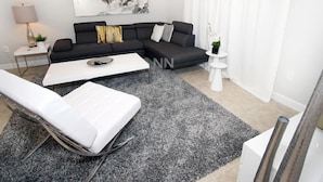 A modern living room with a sectional sofa, a white coffee table, a grey rug, and a white armchair.