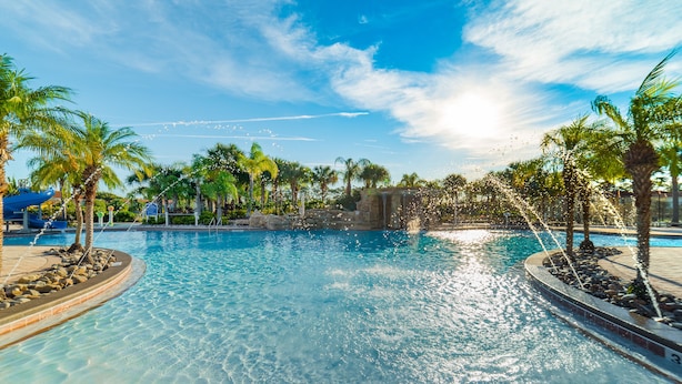A clear blue pool with palm trees and a waterfall feature.