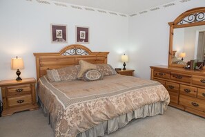 Une chambre à coucher avec un grand lit, une tête de lit en bois, deux tables de chevet avec des lampes, une commode et un miroir.