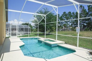 Une piscine extérieure couverte, protégée par une structure en verre, entourée d’une pelouse et d’arbres.