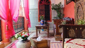 A traditional Moroccan room with a red and white tiled wall, a wooden bed with a red and white patterned bedspread, a small wooden table with a blue vase, and a large mirror with a red frame. - Riad bleu du sud (Marrakech)