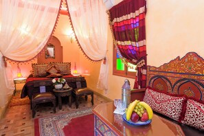 A traditional Moroccan room with a bed, a sofa, a coffee table with fruit, a lamp, and a decorative wall. - Riad bleu du sud (Marrakech)