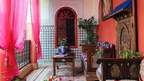 A traditional Moroccan room with a red and white striped ceiling, a wooden sofa, a patterned rug, and a decorative lantern. - Riad bleu du sud (Marrakech)