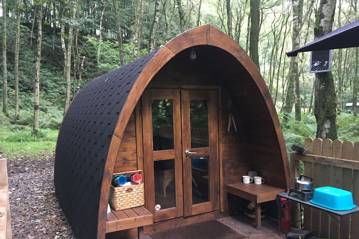 Una cabaña de madera tipo A con una puerta, una mesita y un banco.