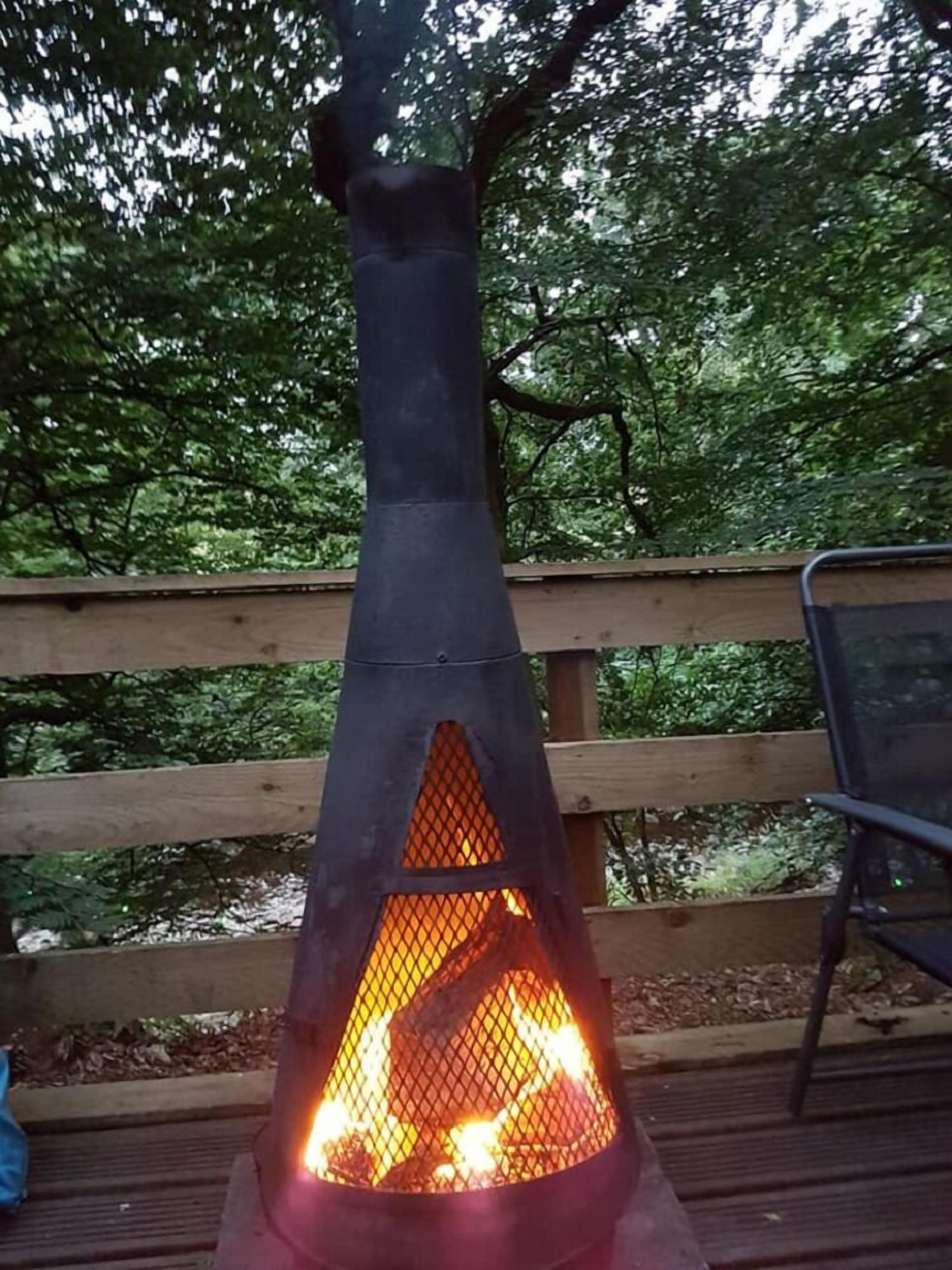A wood-burning stove on a deck with a wooden railing and a chair.