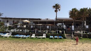A beachside restaurant with outdoor seating, a palm tree, and a child standing on the sand. - Hostal Restaurante Casa Ríos (Tarifa)