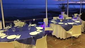 An outdoor dining area with tables set for a meal, overlooking a beach at dusk. - Hostal Restaurante Casa Ríos (Tarifa)