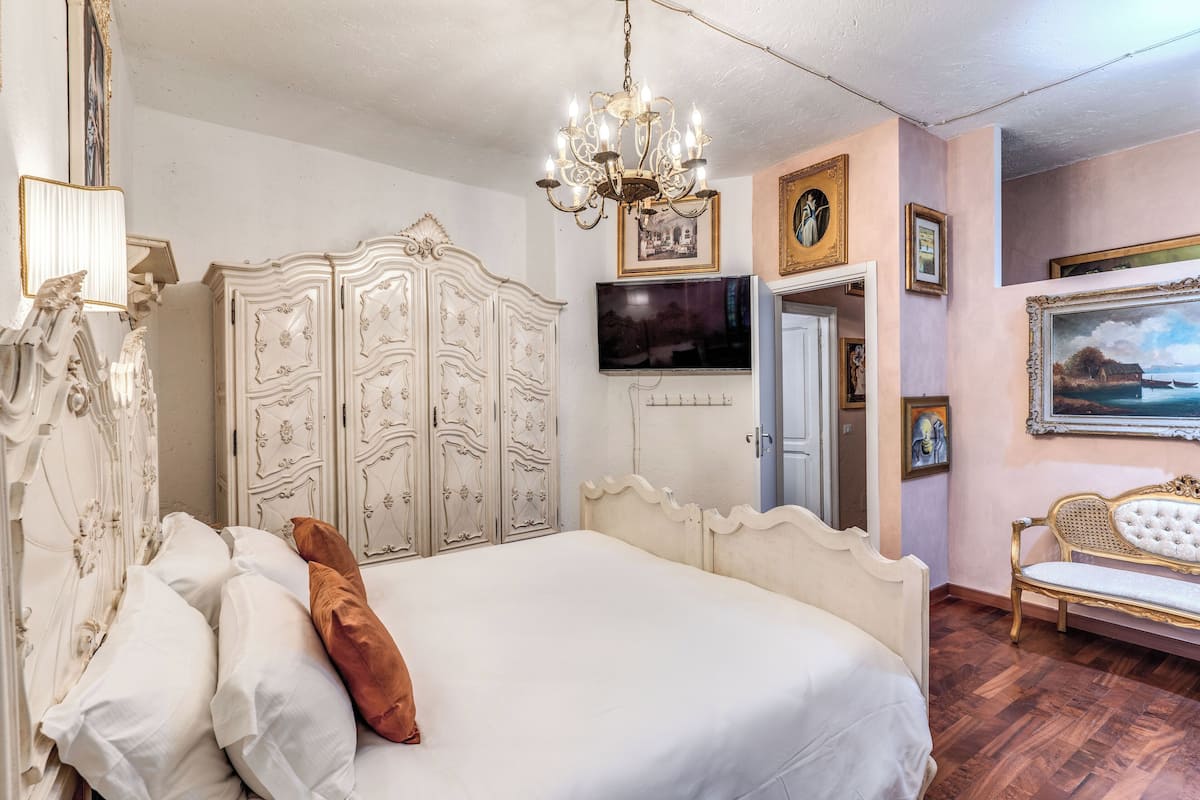 A bedroom with a large bed, a white wardrobe, a television, and a painting on the wall.