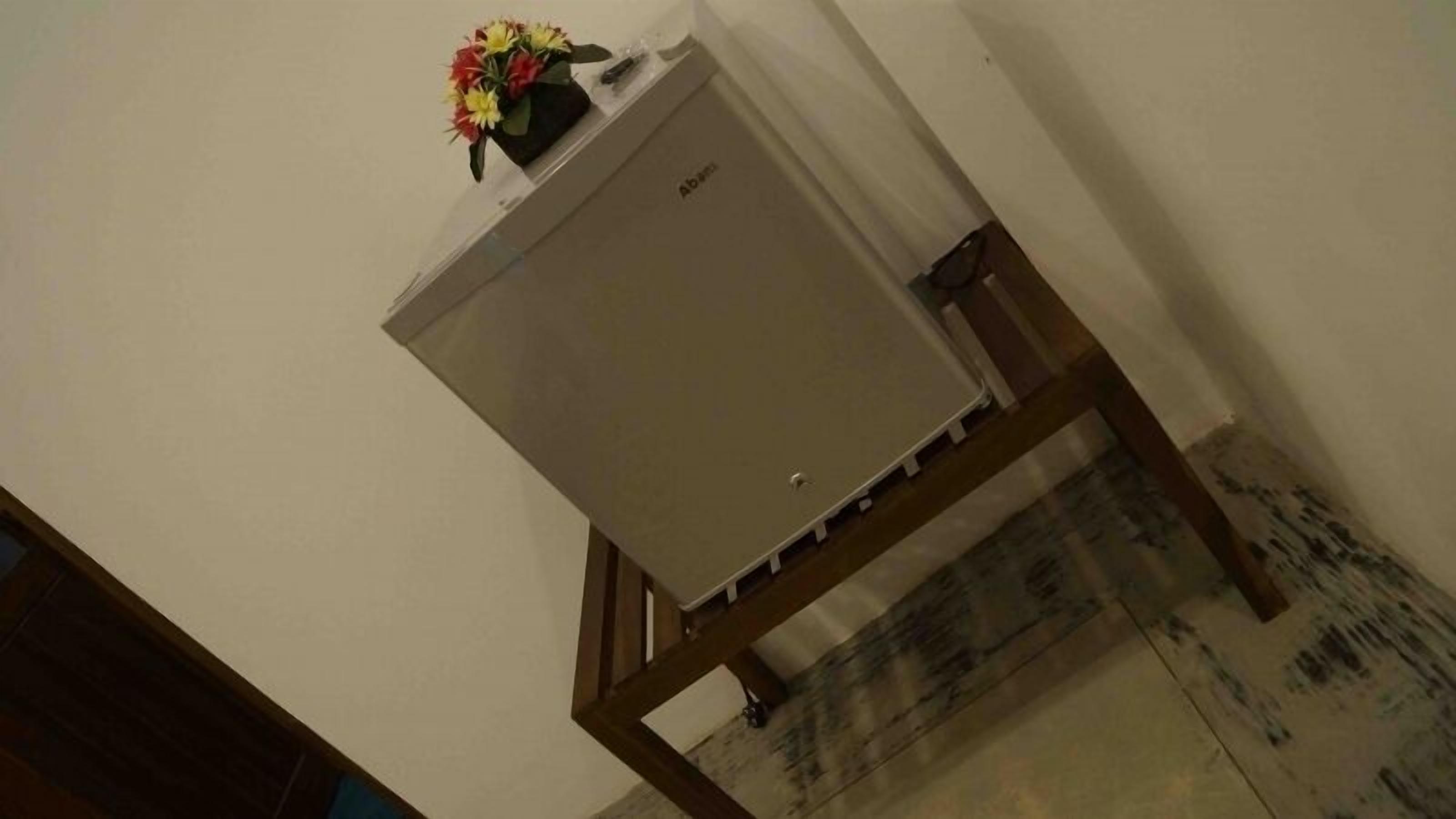 Uma geladeira compacta sobre um suporte de madeira em um quarto com piso de azulejos.