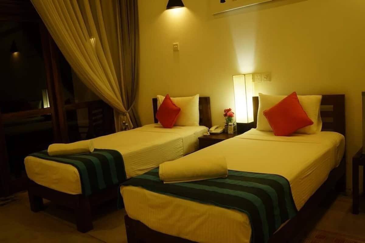 A hotel room with two beds, a nightstand, a lamp, a TV, and a window with curtains.