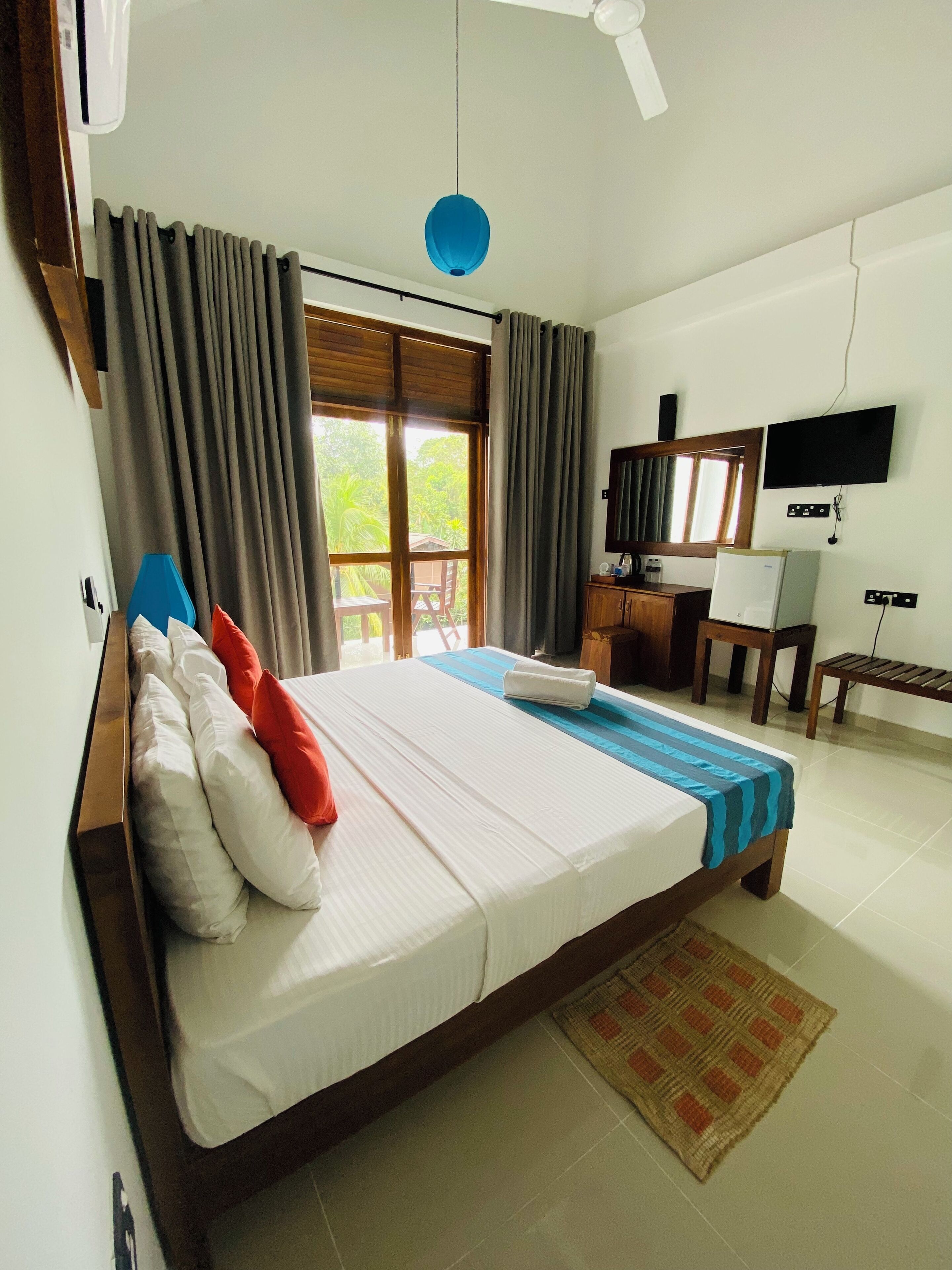 A hotel room with a large bed, a desk with a chair, a television, and a window with curtains.
