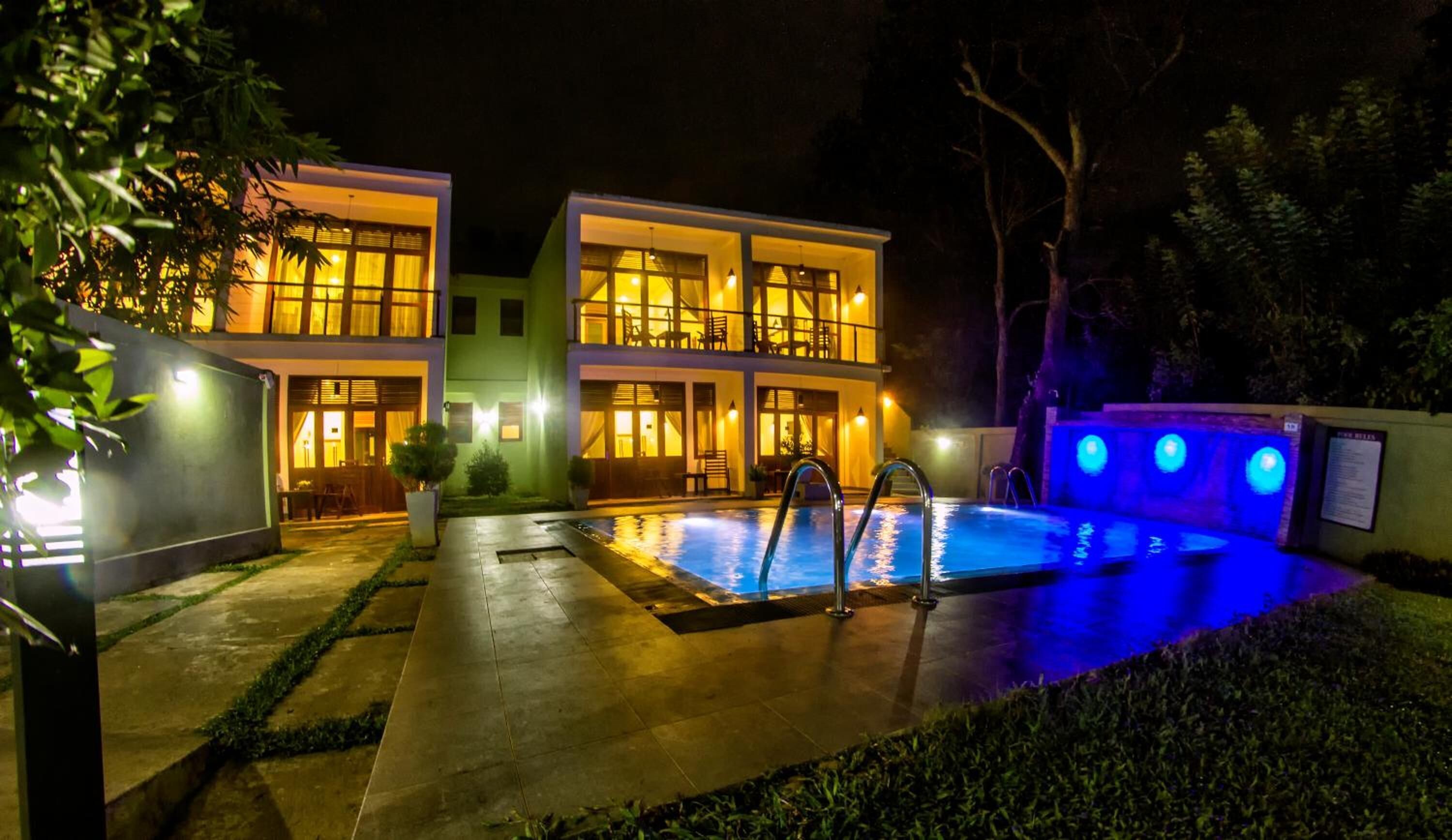 Ein zweistöckiges Gebäude mit Schwimmbad bei Nacht, beleuchtet durch warmes und blaues Licht.
