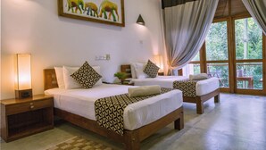 Una habitación de hotel con dos camas, un ventanal con cortinas, un cuadro de elefantes en la pared y una mesita de noche con lámpara.