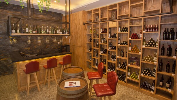 A bar area with wooden shelves stocked with bottles, red chairs, and a bar counter with stools. - Kantel Hotel (Mandalay)