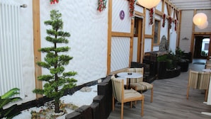 Perinteinen japanilaistyylinen sisustus, jossa on tatamimatto, pieni mänty ja oleskelualue, jossa on tuoleja ja pöytä.