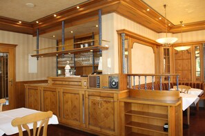 Un hall de hotel tradicional con paneles de madera, una zona de bar con cristalería y una escalera con barandilla azul.