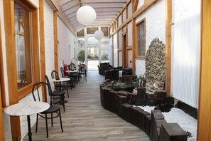 A corridor with wooden flooring, white walls, and a stone feature. Tables and chairs are arranged along the sides. - Hotel am Kurpark (Villingen-Schwenningen)